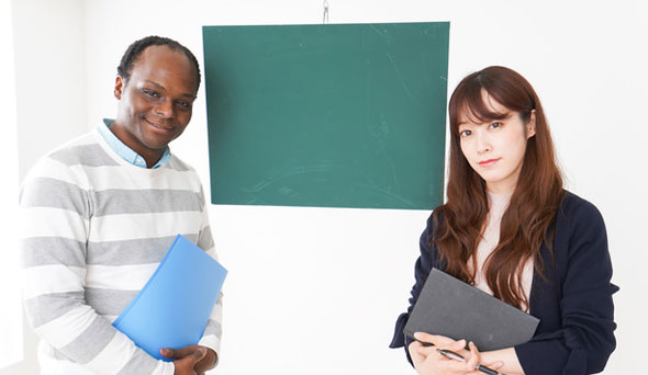 ネイティブ男性講師と日本人女性生徒が黒板の前で向き合っている様子